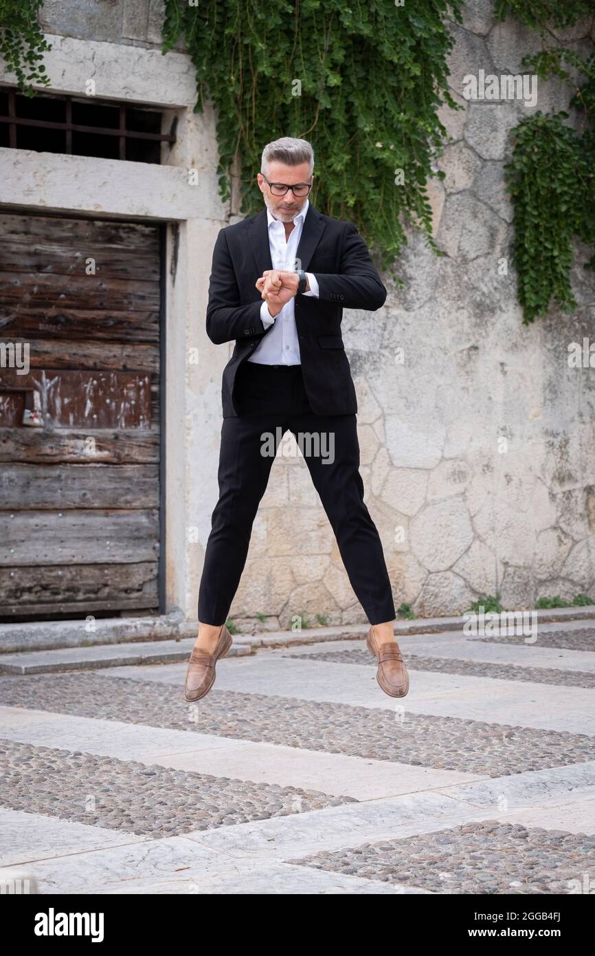 Handsome businessman checking the time on his watch and jumping from stationary. Strange and surreal situation Stock Photo