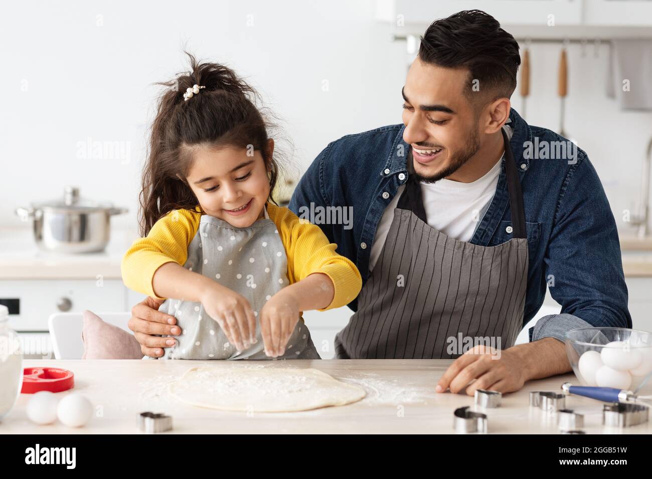 Cheerful arab dad and little daughter baking together in kitchen, making pizza Stock Photo