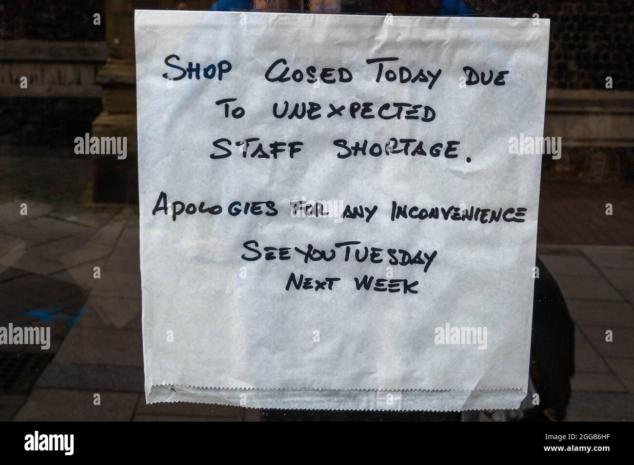A white paper bag taped to a window stating that the shop is closed due to staff shortages Stock Photo