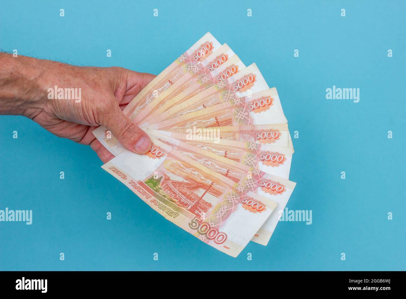 male hand male hand holding bills on a blue backgroundholding bills on a blue background Stock Photo