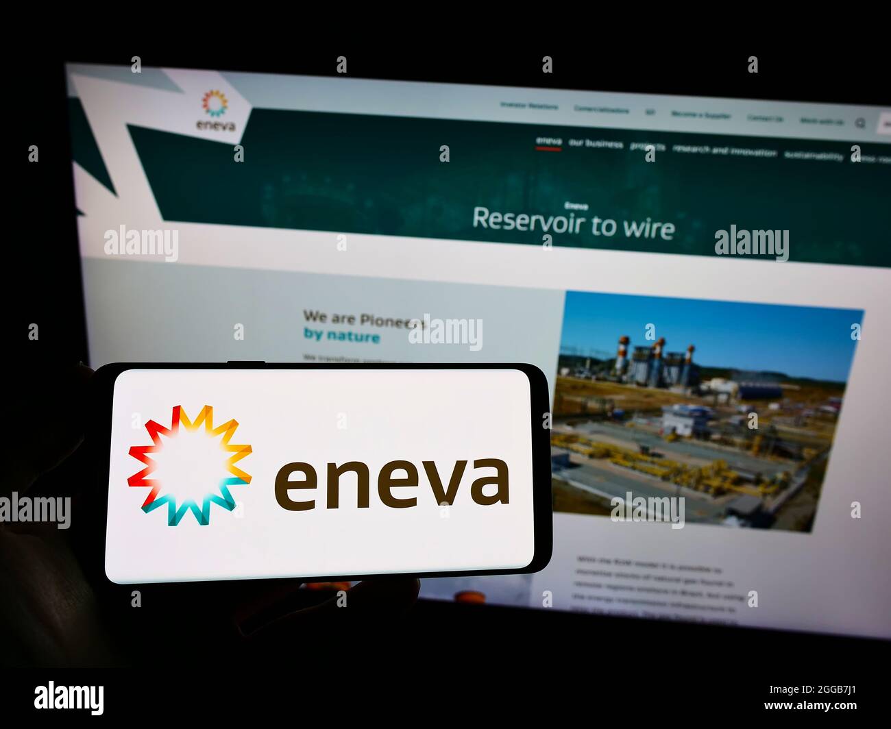 Person holding cellphone with logo of Brazilian power generation company Eneva SA on screen in front of business webpage. Focus on phone display. Stock Photo