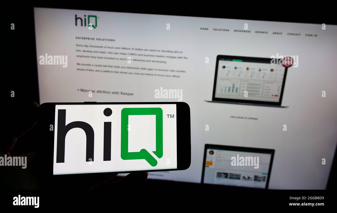 Person holding mobile phone with logo of American data science company hiQ Labs Inc. on screen in front of web page. Focus on phone display. Stock Photo