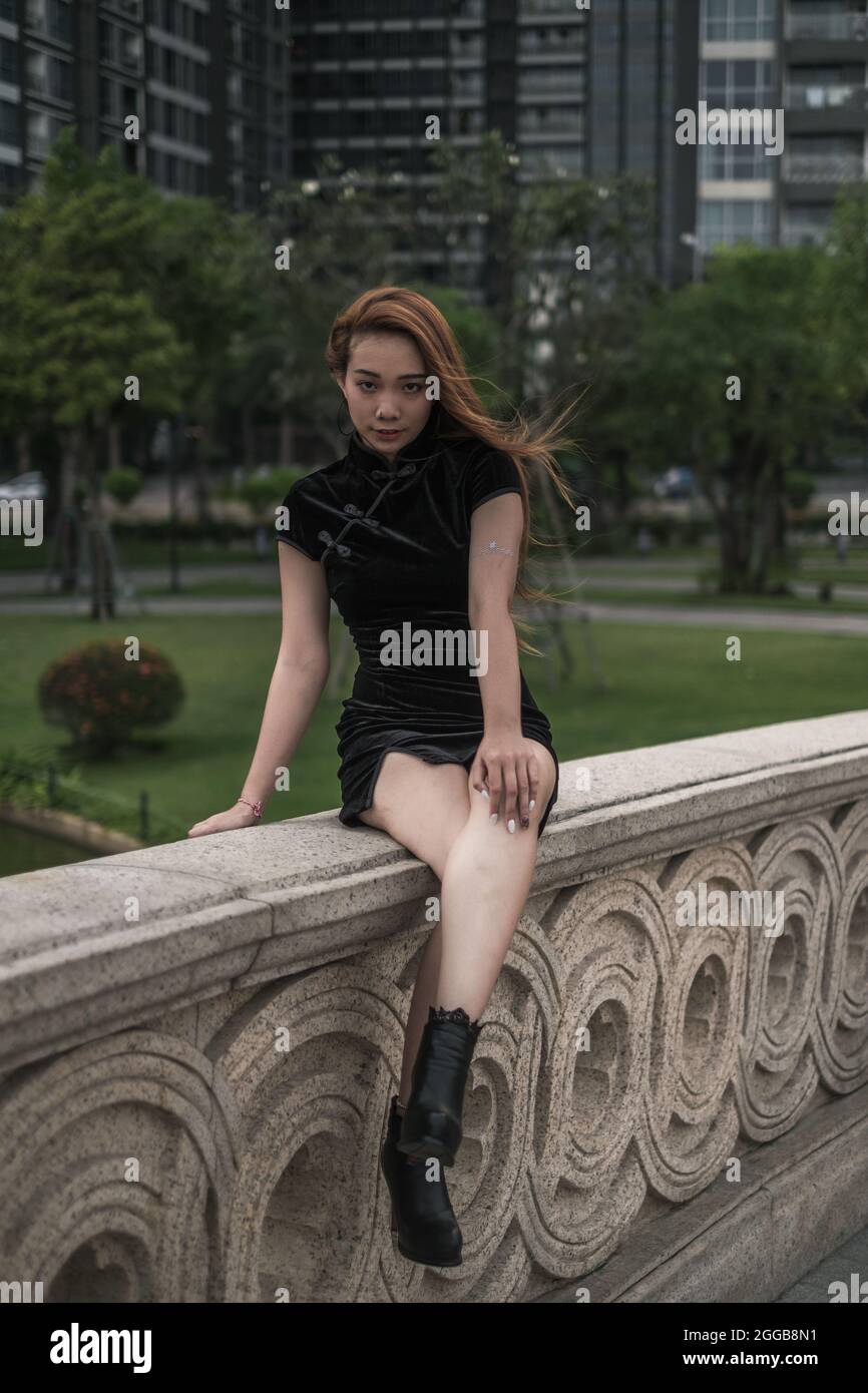 Beautiful young asian woman in casual black dress sitting on handrail ...
