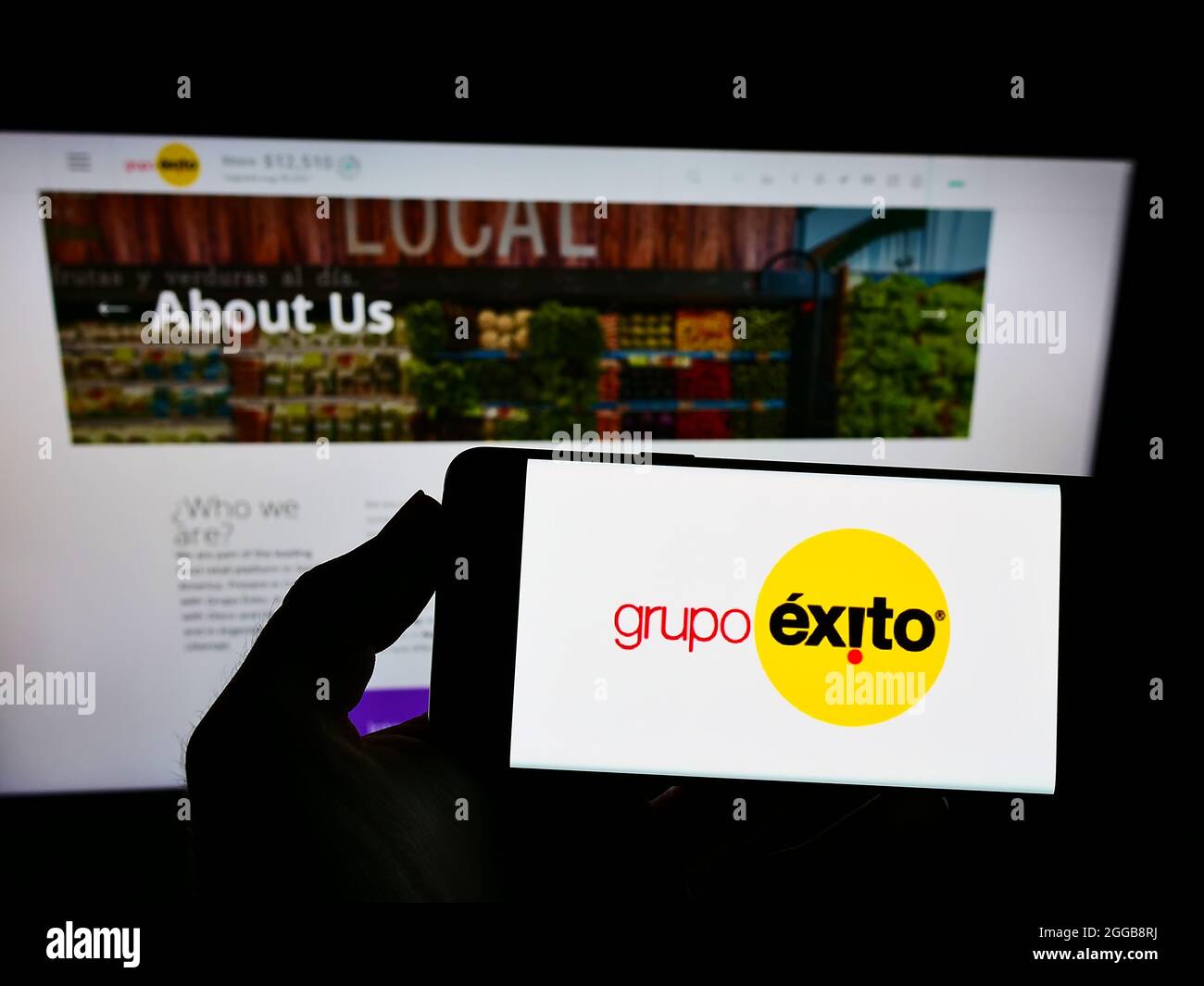 Person holding smartphone with logo of company Almacenes Éxito S.A. (Grupo Éxito) on screen in front of website. Focus on phone display. Stock Photo