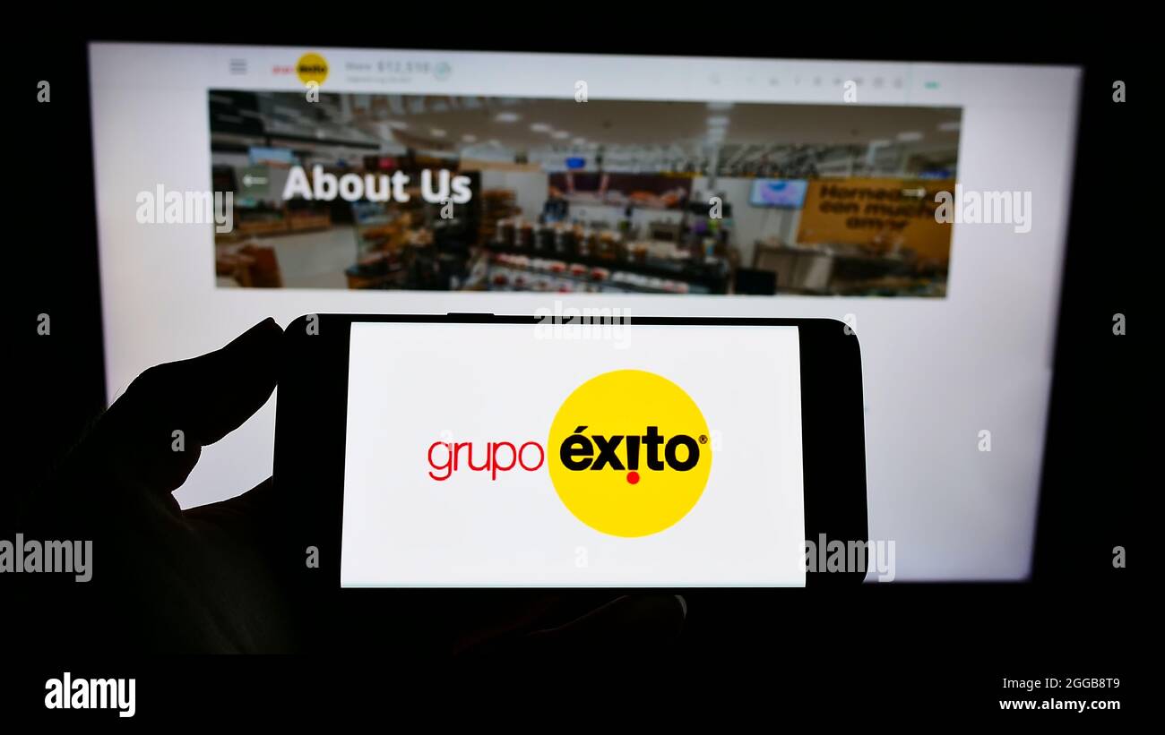 Person holding cellphone with logo of company Almacenes Éxito S.A. (Grupo Éxito) on screen in front of business webpage. Focus on phone display. Stock Photo