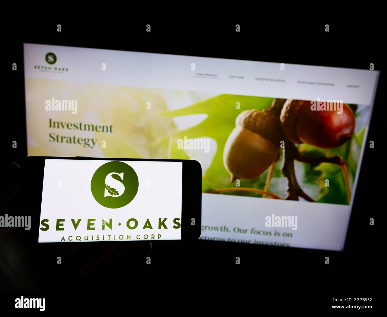 Person holding mobile phone with logo of US company Seven Oaks Acquisition Corp. on screen in front of business web page. Focus on phone display. Stock Photo