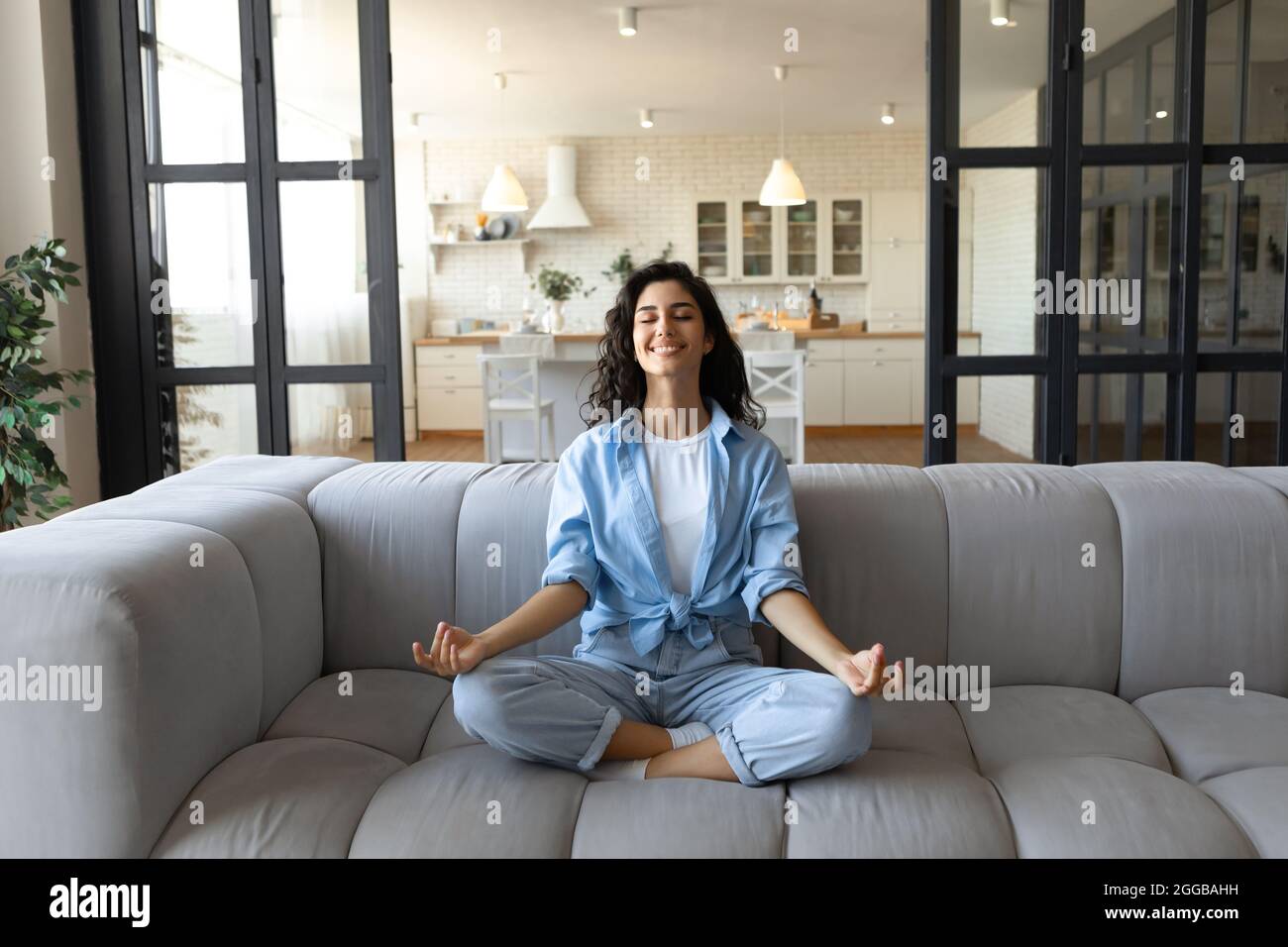 Stress management. Peaceful young lady in casual wear meditating with closed eyes on couch at home Stock Photo