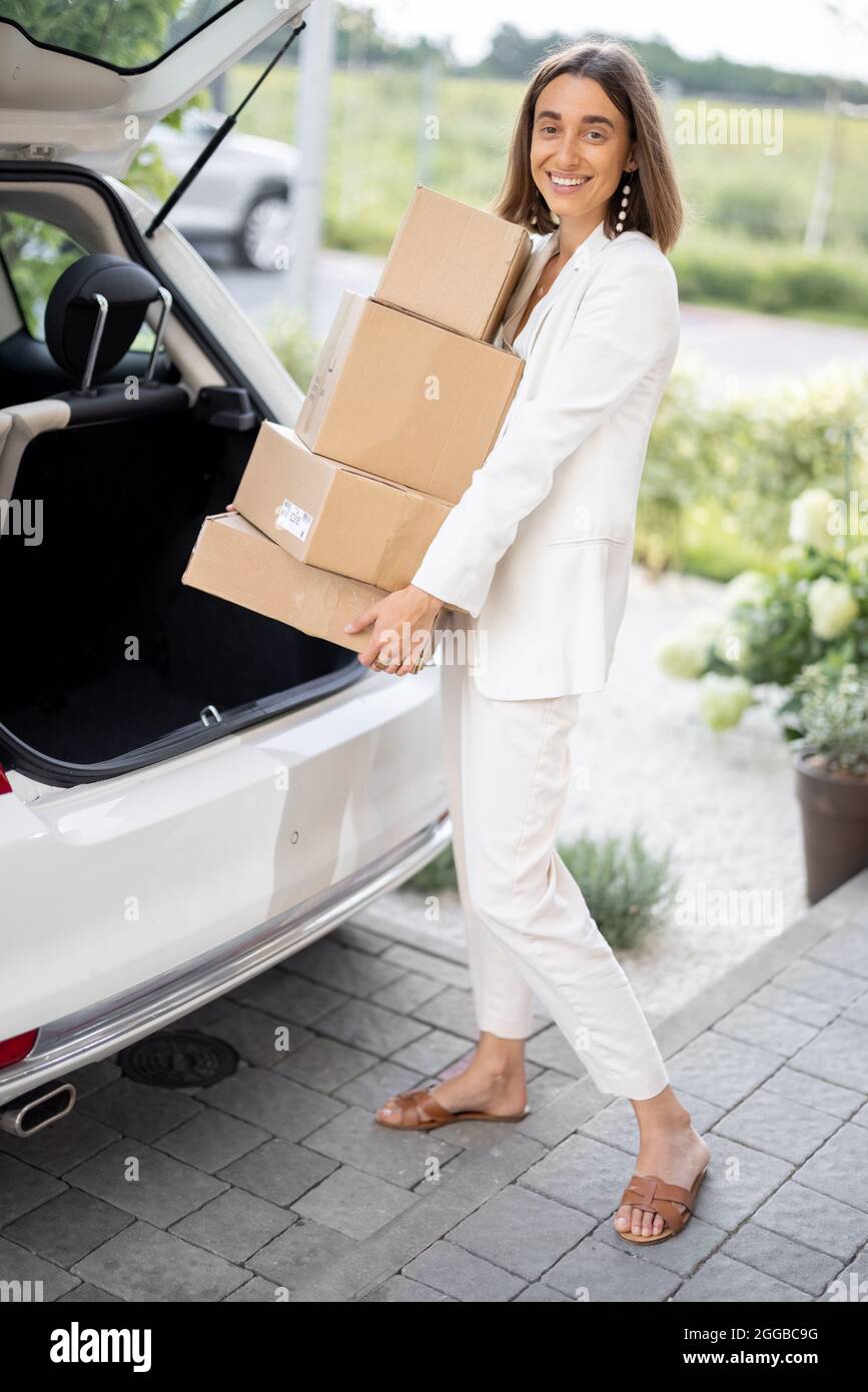 Woman picking up a parcels from a car trunk near a house Stock Photo