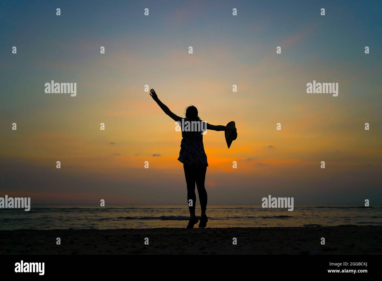 Rear view silhouette of young woman dancing at sunset on a UK beach ...
