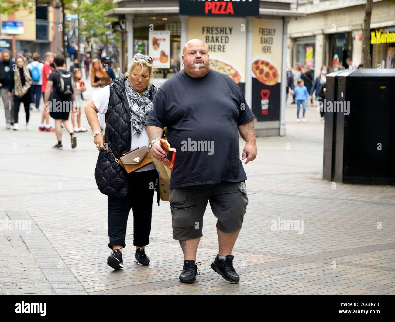 Very obese man, eating pizza in the street Stock Photo