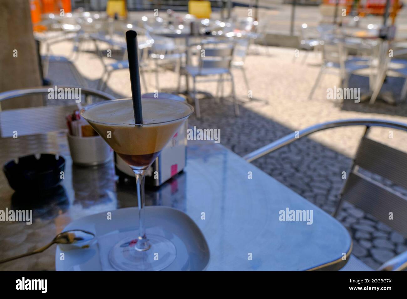 Ice coffee, cafe shakerato in glass close-up on the table across restaurant furniture and city view. Stock Photo
