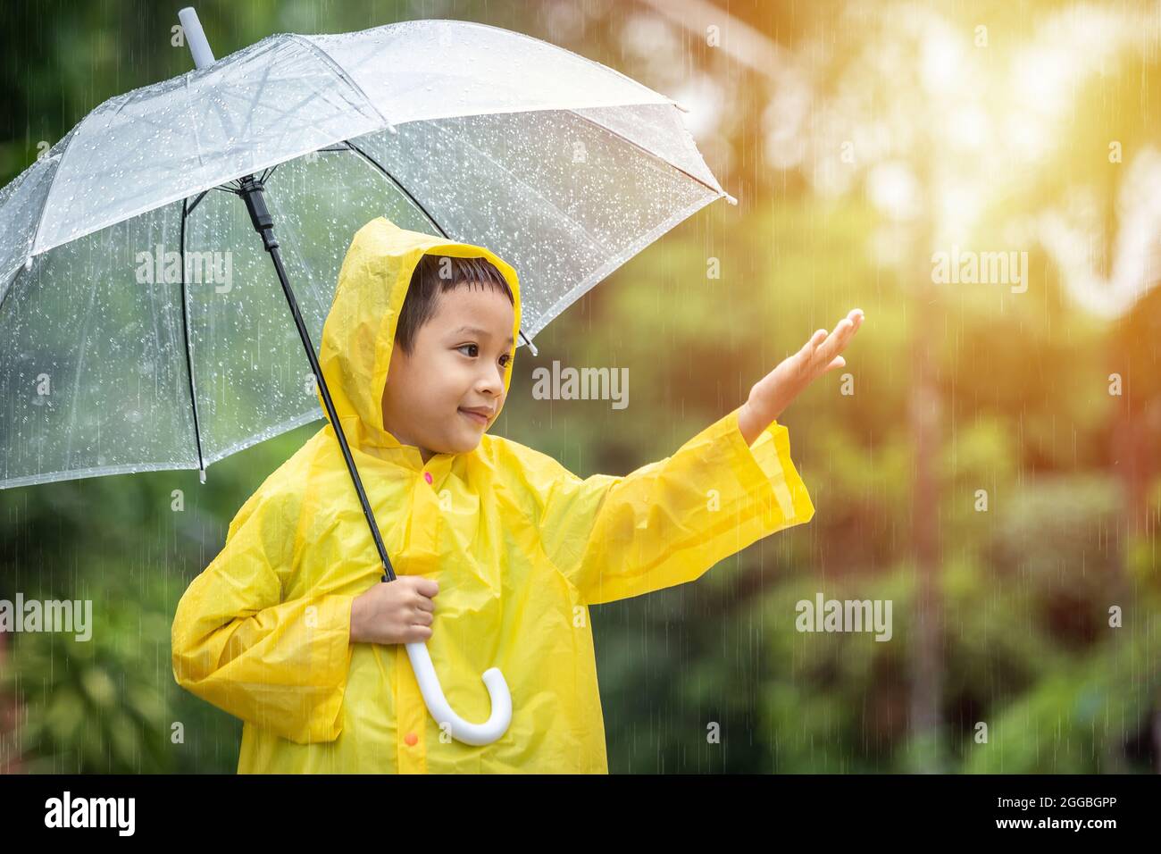 Asian kid holding an umbrella and catching raindrops. Happy Asian little child boy having fun playing with the rain in the evening sunlight. Stock Photo