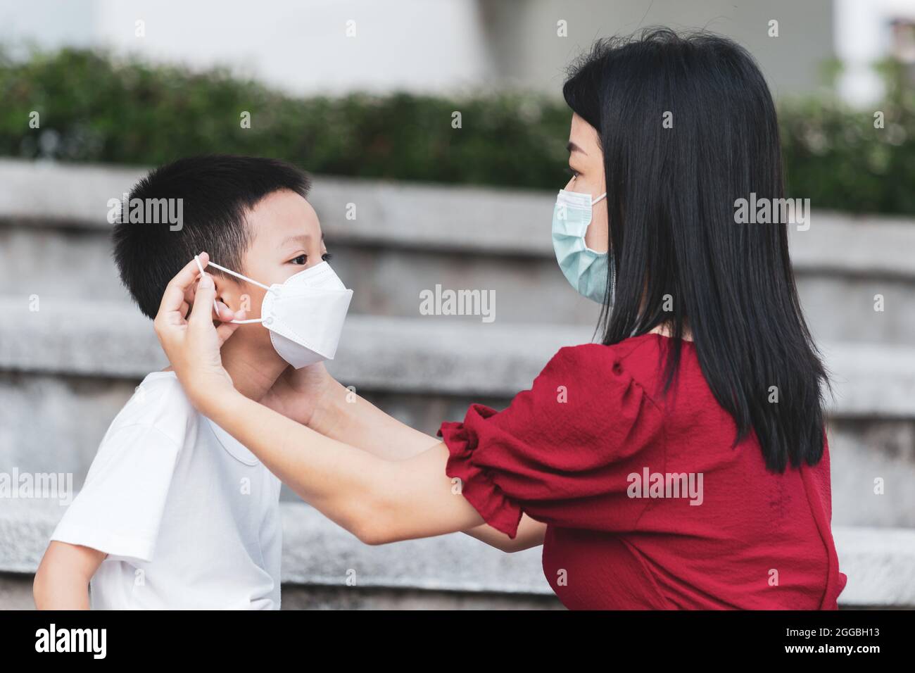 Mom is wearing a medical mask for her child. Little Asian boy and mom in the medical mask. Asian family protection virus concept. Stock Photo