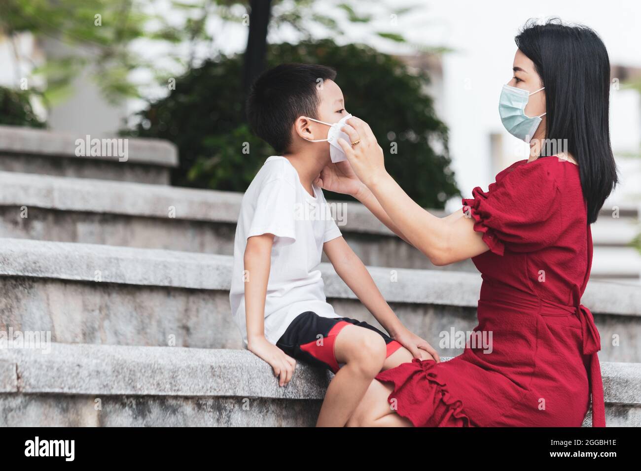 Mom is wearing a medical mask for her child. Little Asian boy and mom in the medical mask. Asian family protection virus concept. Stock Photo