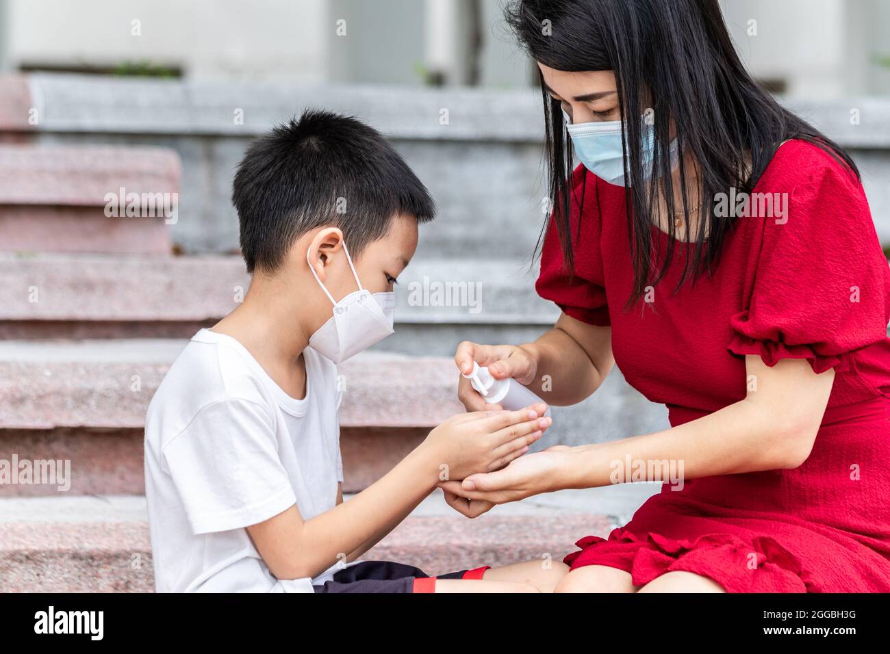 Mom and son wearing a medical mask during coronavirus and flu outbreak. Little Asian boy and mom wash their hand with alcohol gel. Asian family Stock Photo