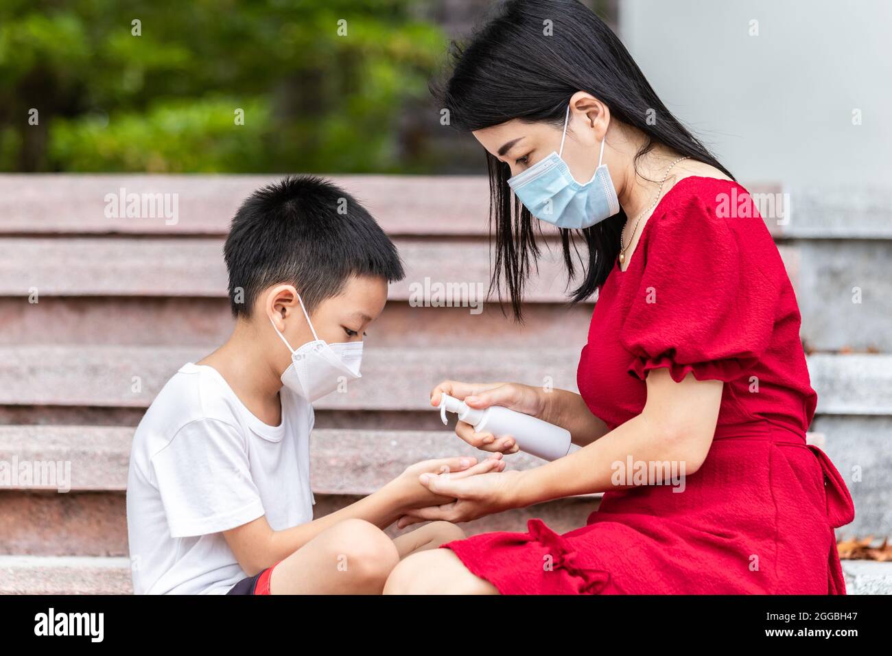 Mom and son wearing a medical mask during coronavirus and flu outbreak. Little Asian boy and mom wash their hand with alcohol gel. Asian family Stock Photo
