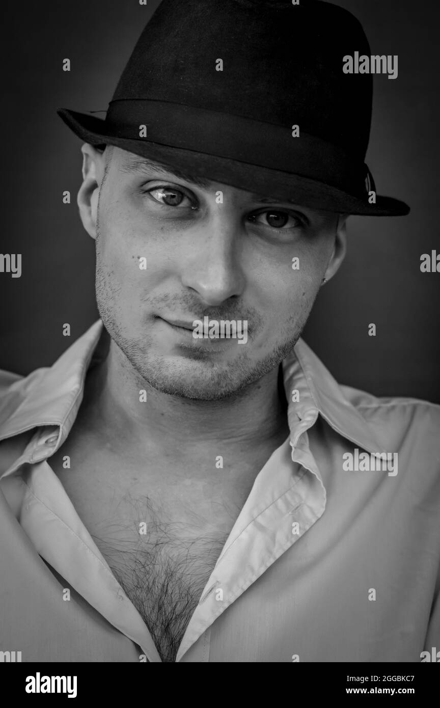 black and white portrait of a young man in a black hat and shirt looking intently at the camera Stock Photo
