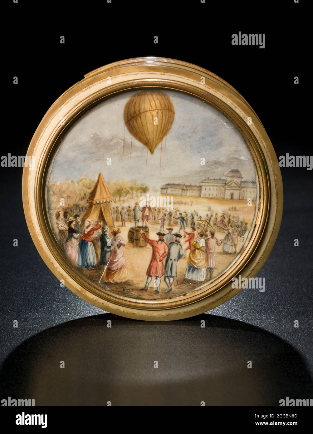 Snuff box with ballooning scene, late 18th century. The scene represents the launch of the first small Charliere gas balloon from the Champ de Mars in Paris, 27 August 1783. A small applauding crowd is gathered, and two men are shaking hands. The hydrogen generating barrels are shown. Round ivory snuff box with a ballooning scene painted on ivory set into the lid. The painting is signed 'Aubert,' and is under glass in a copper alloy frame. The box is made from multiple pieces of ivory glued together. Bands of a different shade of ivory are inset into the edges of the box. Stock Photo