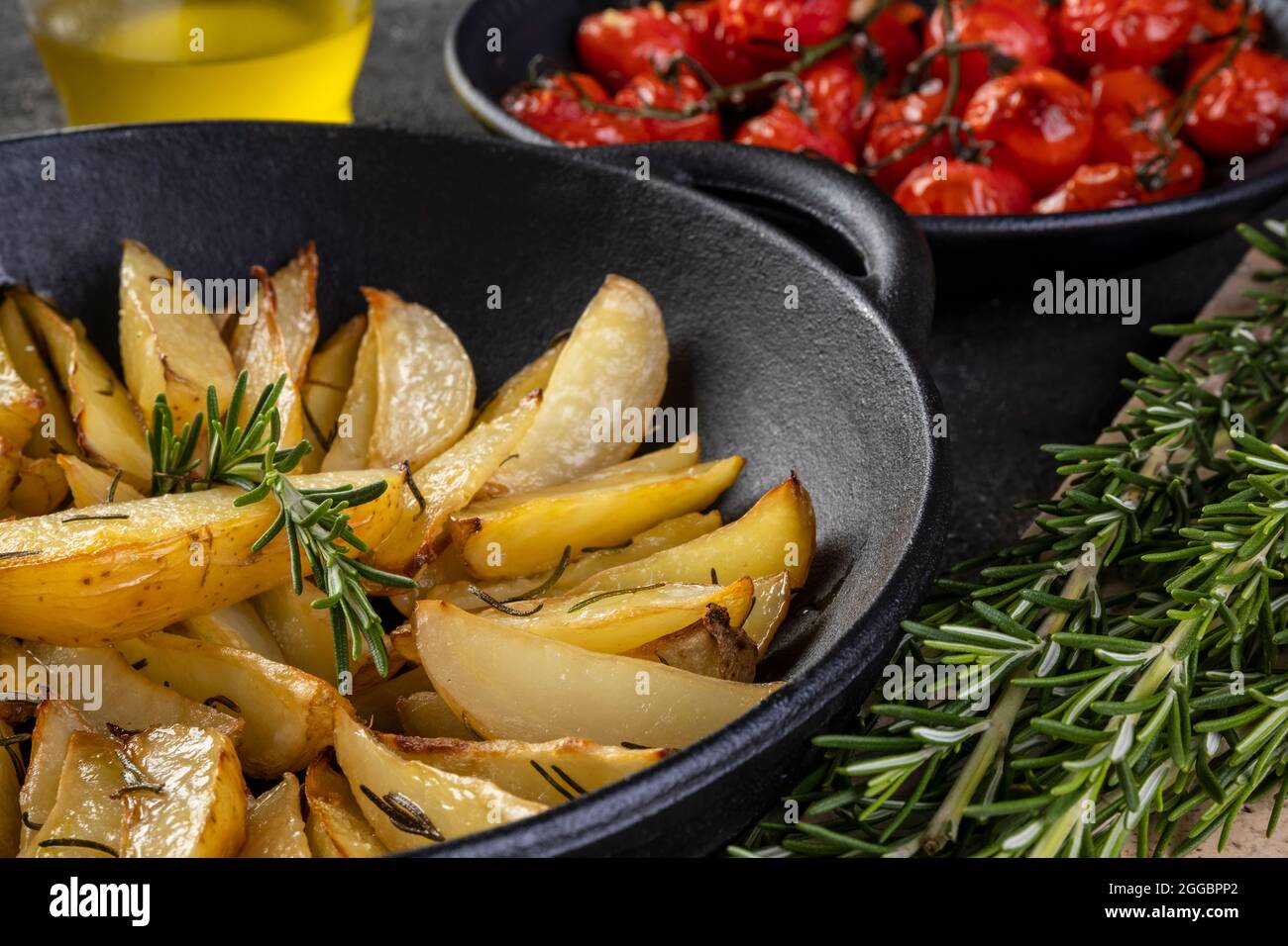 https://c8.alamy.com/comp/2GGBPP2/roasted-potatoes-with-rosemary-in-iron-casserole-and-plate-of-confit-tomatoes-on-dark-background-2GGBPP2.jpg
