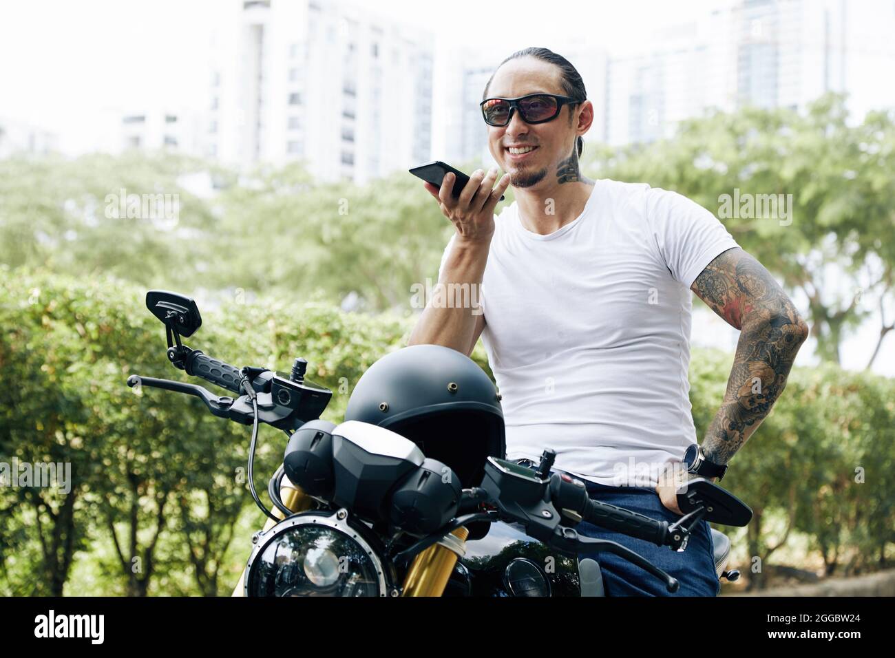 Happy fit man sitting on motorcyle and recording voice message for friend Stock Photo