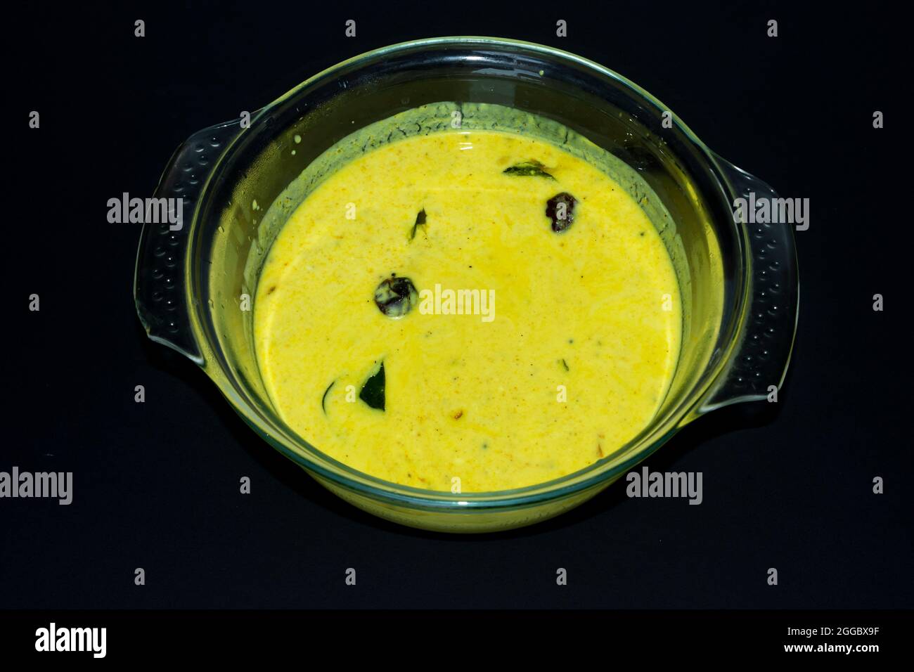 Closeup Image Of Kerala Onam Special Traditional Yellow Buttermilk Curry Also Known As Moru Curry, Pulissery, Kachiya Moru In Glass Bowl. Black Backgr Stock Photo