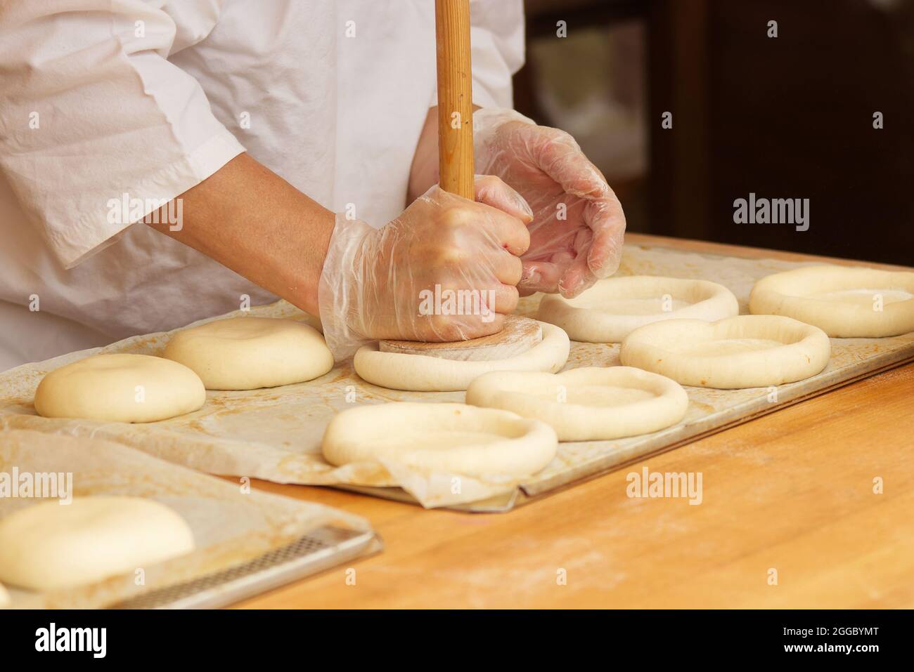 The woman in the picture is making stuffed pies. Hands in protective gloves holding the tool press dough to get the proper shape of pie. Work in the b Stock Photo