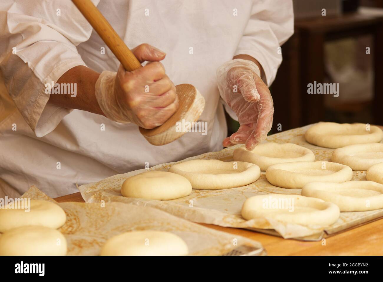 The woman in the picture is making stuffed pies. Hands in protective gloves holding the tool press dough to get the proper shape of pie. Work in the b Stock Photo