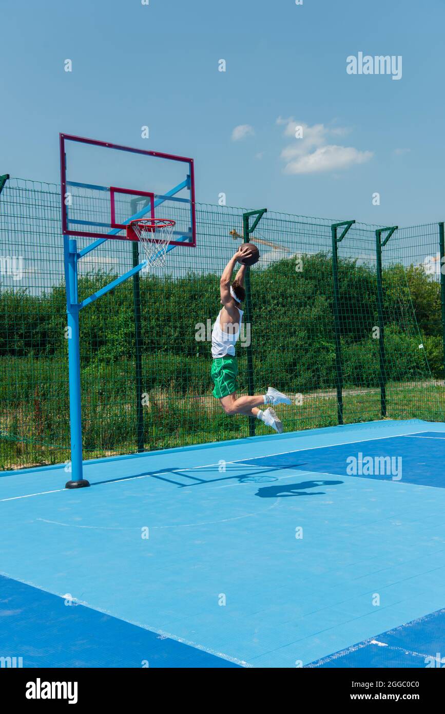 Young sportsman with basketball ball jumping under hoop on playground
