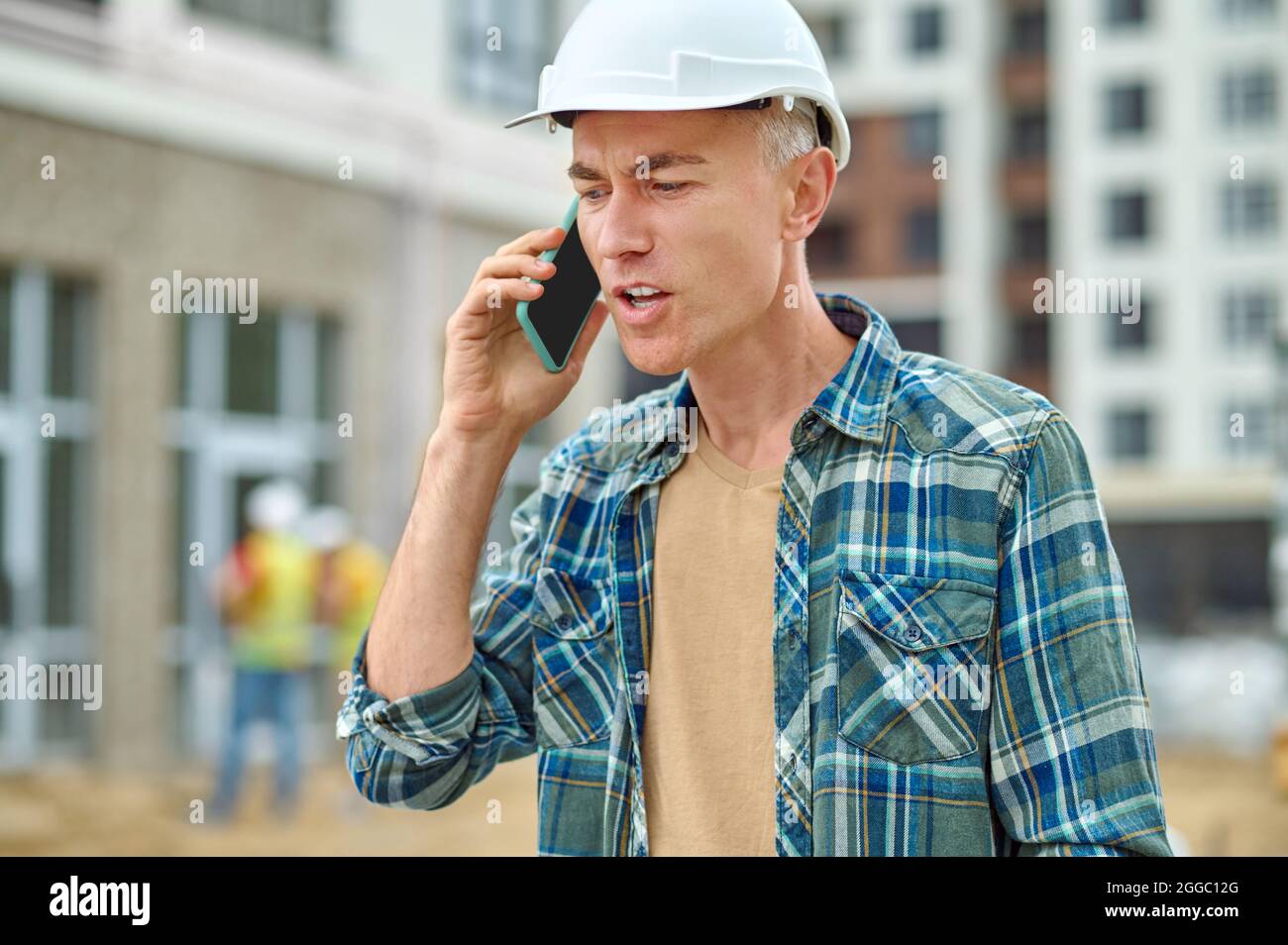 Gray-haired male builder talking on his cellphone outdoors Stock Photo