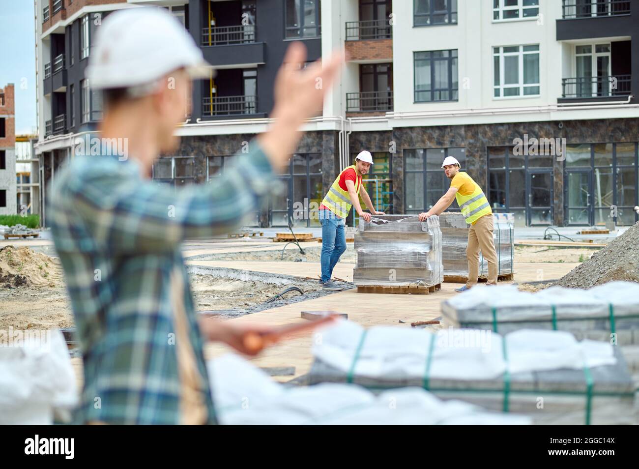 Two young builders looking at their colleague waving at them Stock Photo