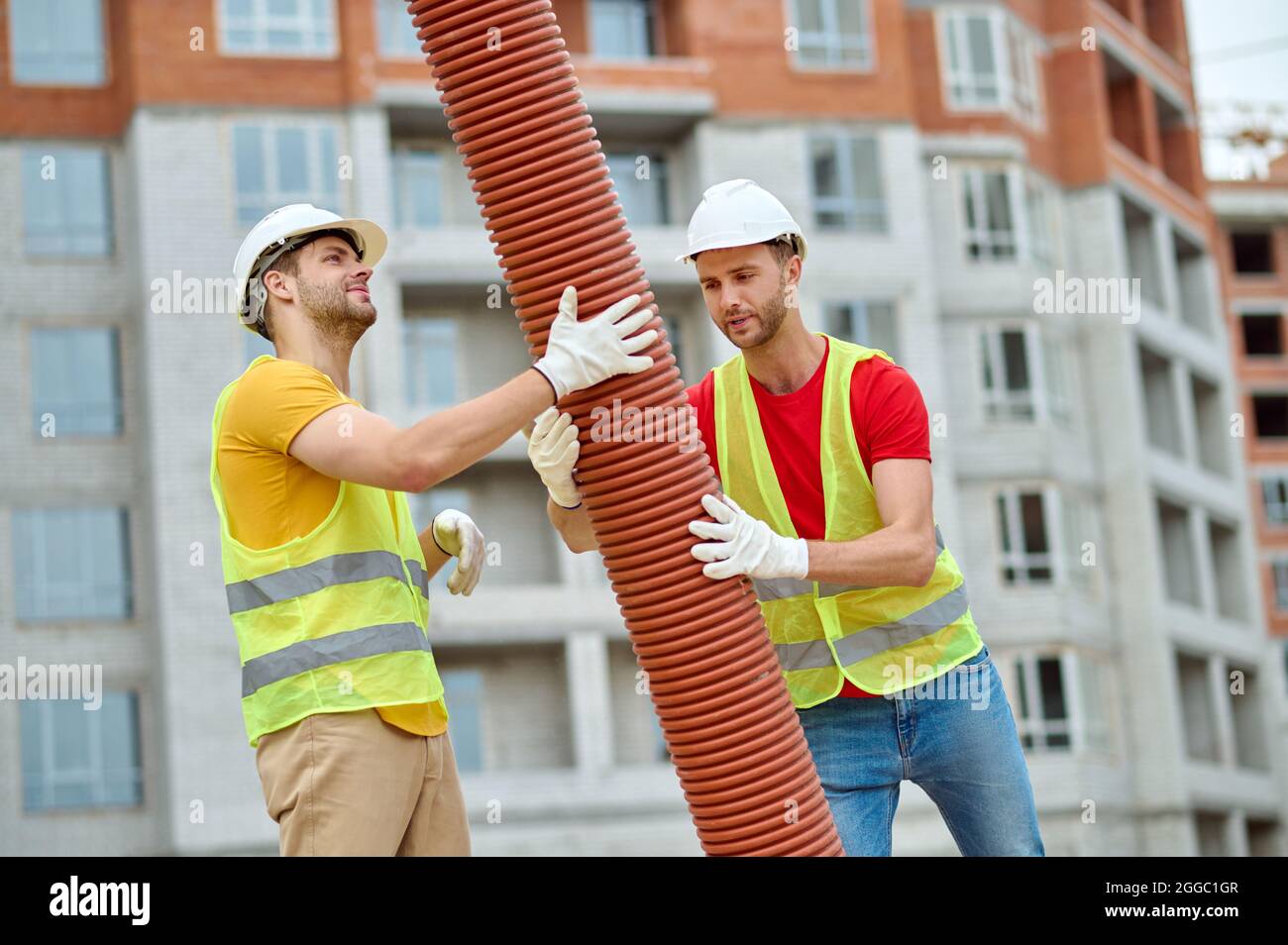 Experienced Caucasian workers in hardhats installing a drainage system Stock Photo