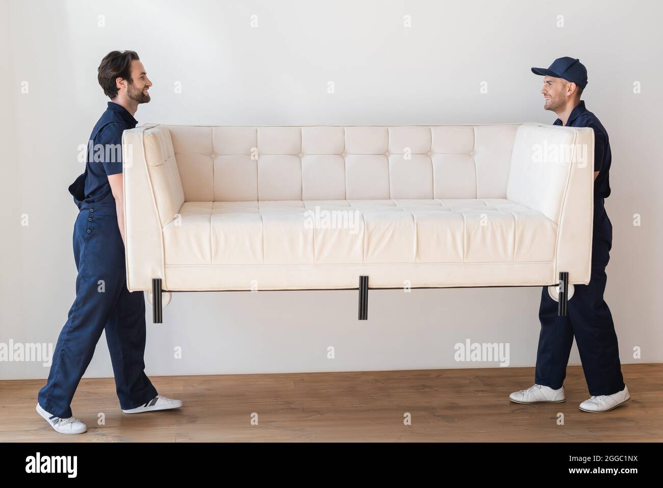 side view of movers carrying white couch in living room Stock Photo Alamy