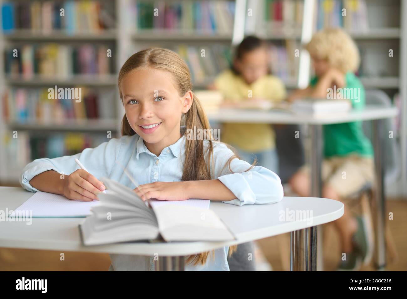 Pleased pupil with a ball-point pen seated at the desk Stock Photo