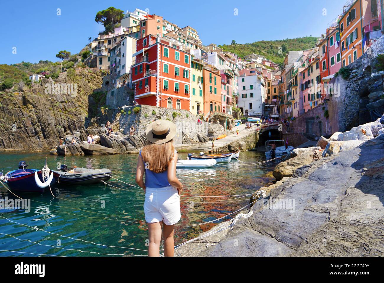 Vacation in Europe. Beautiful woman walking in Riomaggiore harbor looking at picturesque village overhanging cliffs, Cinque Terre, Italy. Stock Photo