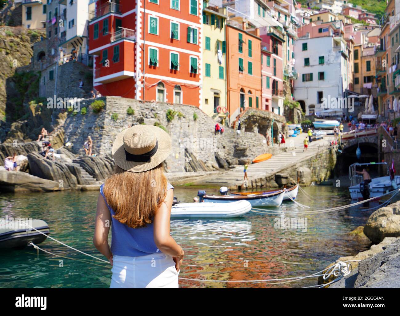 Holidays in Italy. Pretty young woman looking at the village of Riomaggiore from the harbor, Cinque Terre, Italy. Stock Photo