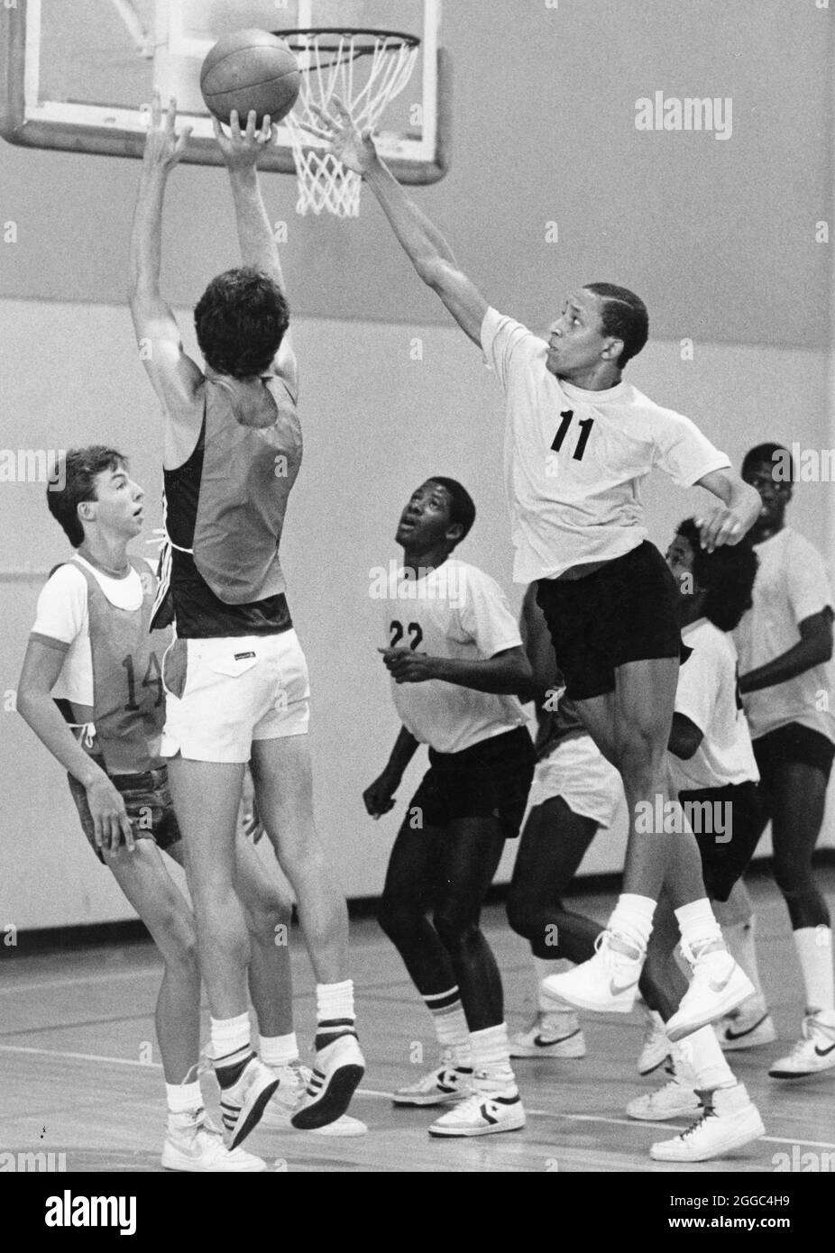 ©1980's Boys high school basketball gam, one boy attempts to block the shot of another during playoff contest. Stock Photo