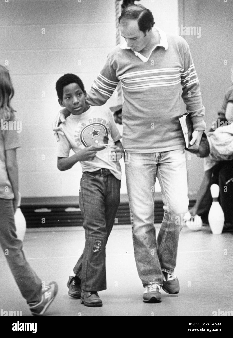 Austin Texas USA, 1984: Black fourth grade student Patrick Skeaton, who lost his right leg due to spina bifida, interacts with his teacher during physical education class at Wooten Elementary School while walking on his new prosthetic leg. ©Bob Daemmrich Stock Photo