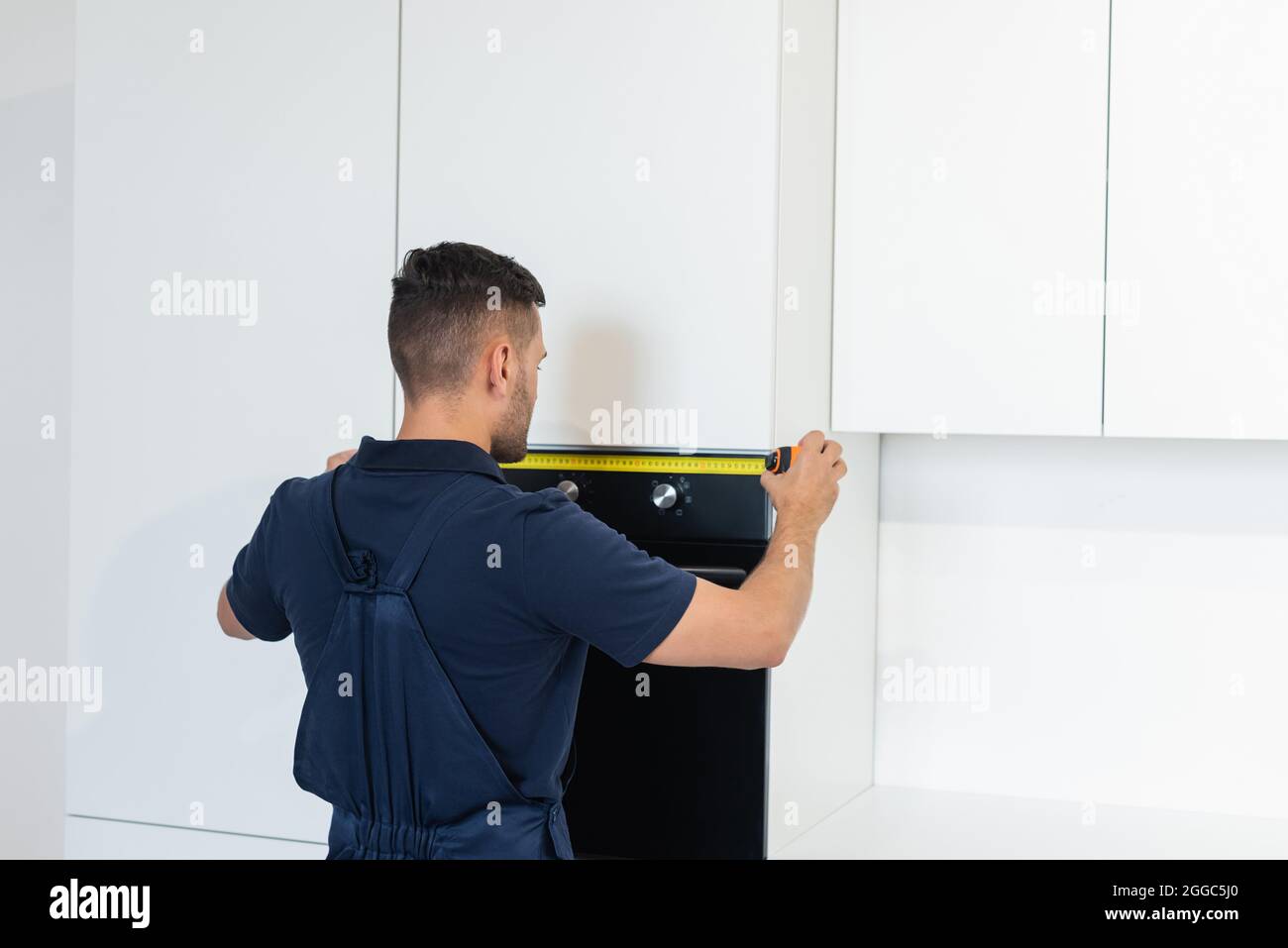 workman measuring electric built-in oven in modern kitchen Stock Photo