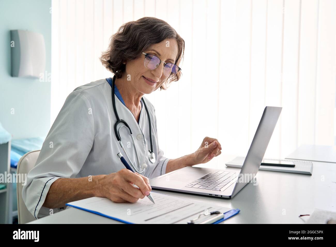 Senior female doctor in clinic consulting remotely using pc laptop computer. Stock Photo