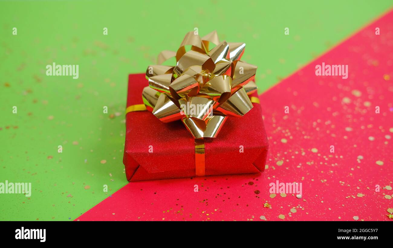 Red gift box with golden ribbon with golden sparkles on the green and ...
