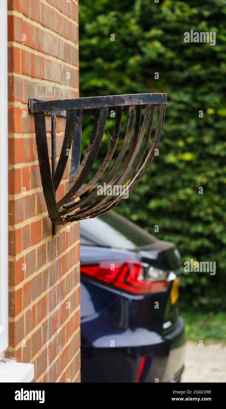 a large black metal flower container on a brick wall with car and hedgerow as background Stock Photo