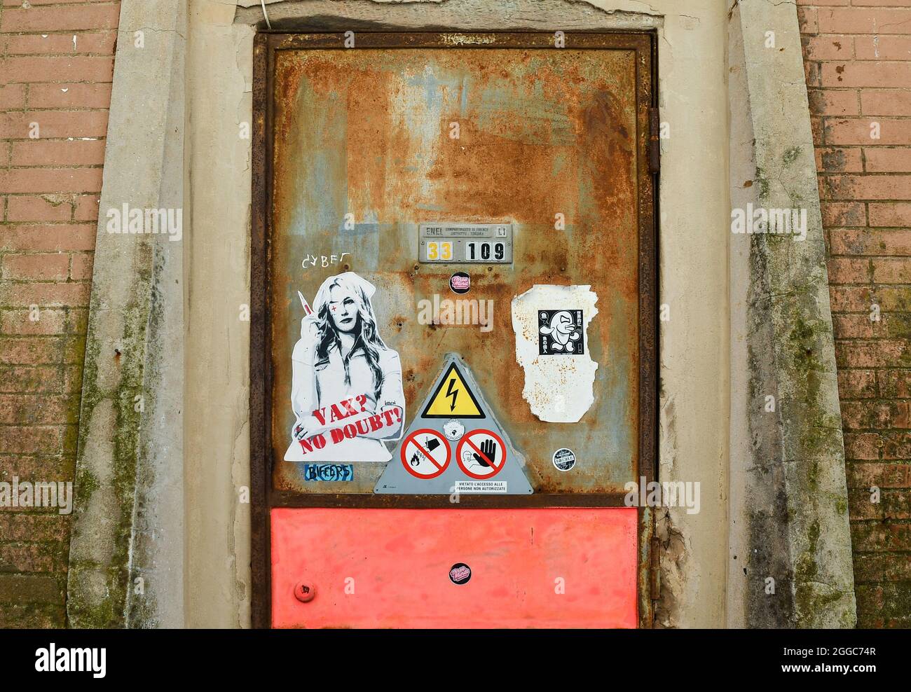 Rusty door of an old power station with the paste-up artwork 'Vax? No doubt!' by street artist Laben and a little sticker by Merioone, Livorno, Italy Stock Photo