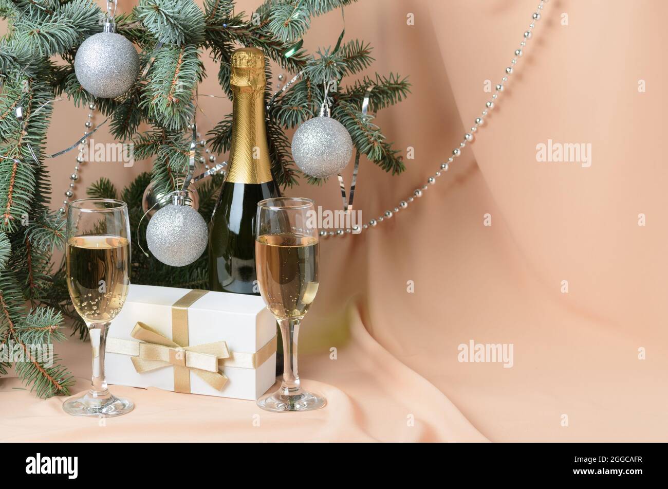 Christmas. A New Year's composition made of branches of a Christmas tree decorated with silver balls, a gift box, sparkling wine glasses on a backgrou Stock Photo