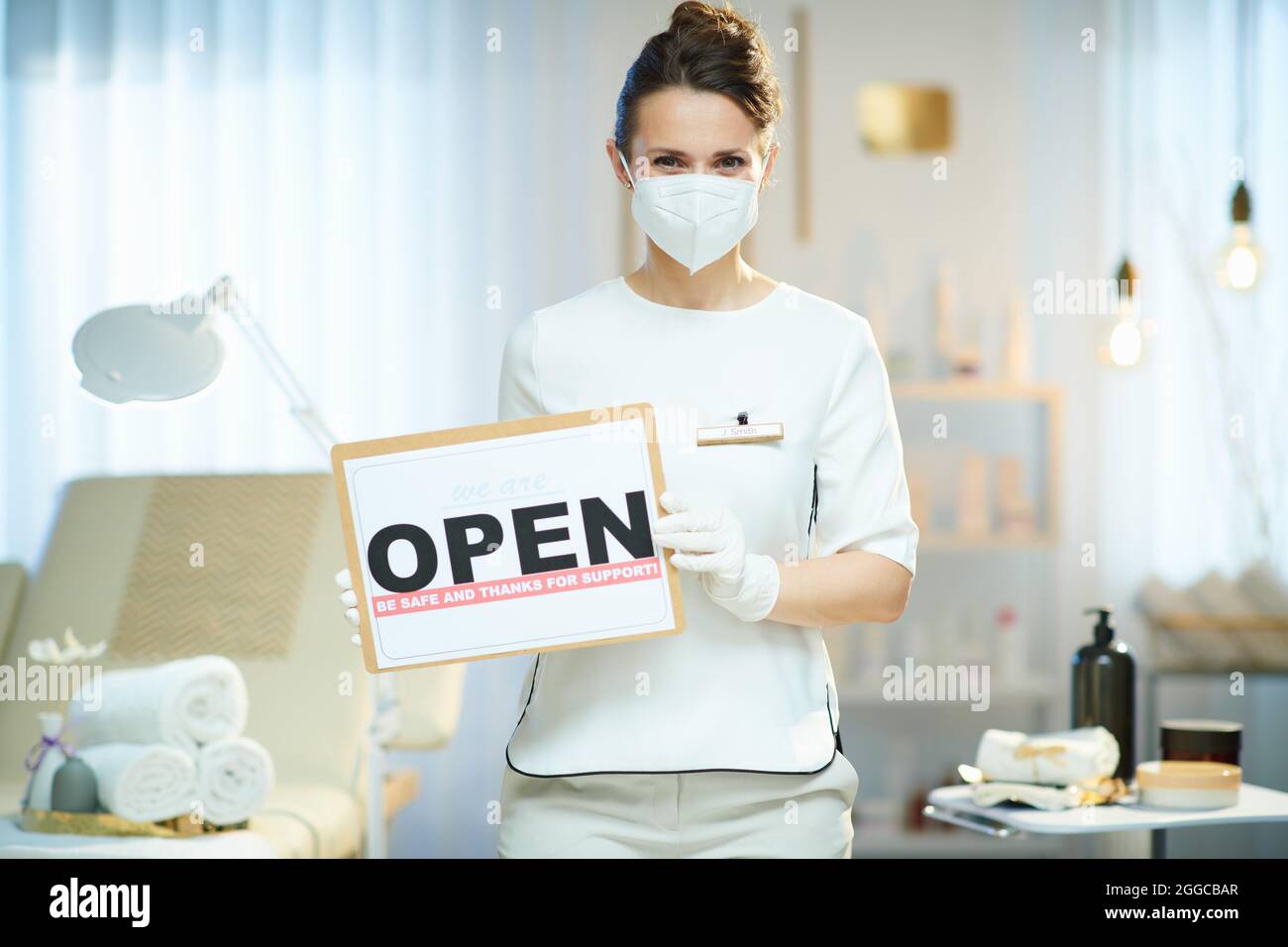 Business during covid-19 pandemic. female employee with ffp2 mask and open sign in modern beauty studio. Stock Photo