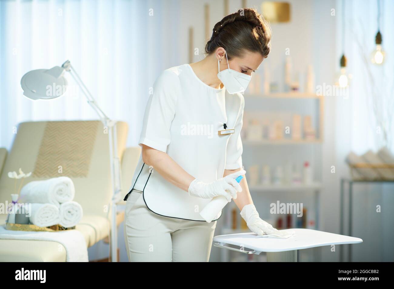 Business during coronavirus pandemic. 40 years old woman employee with ffp2 mask and an antibacterial agent in modern beauty studio. Stock Photo