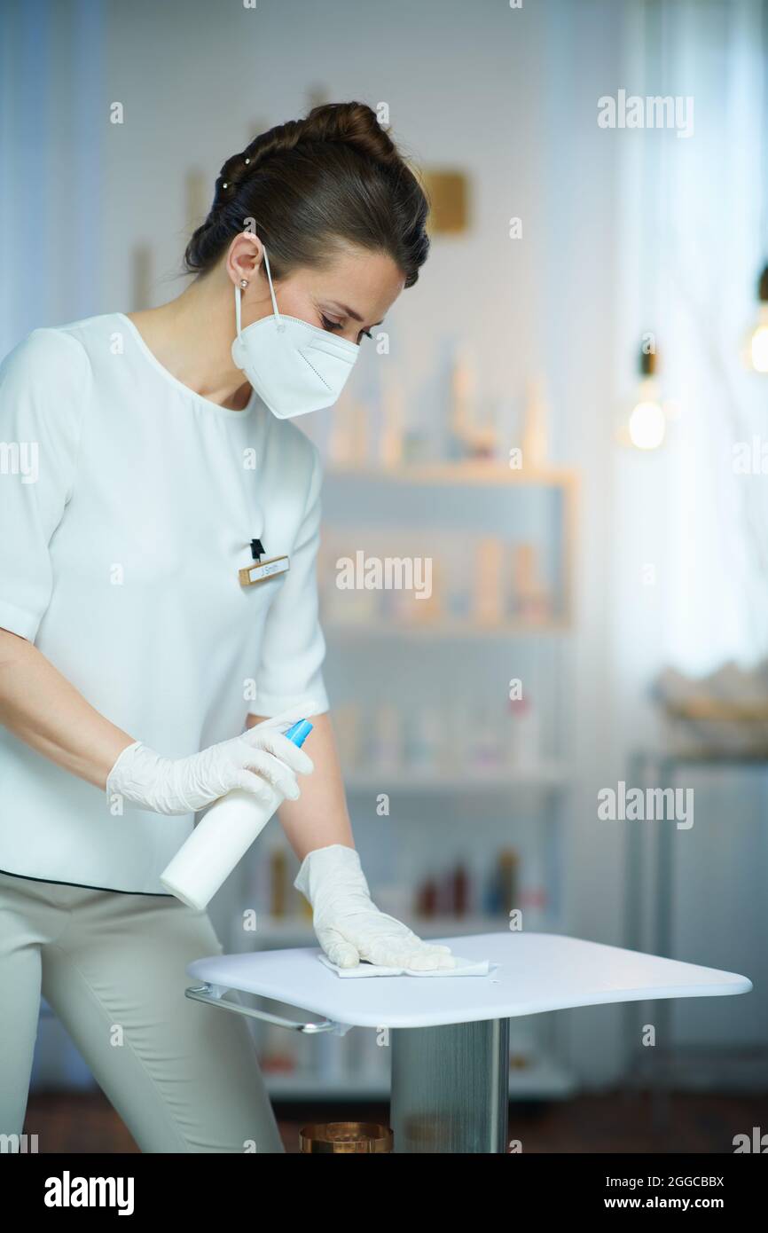 Business during coronavirus pandemic. 40 years old woman worker with ffp2 mask and disinfectant in modern beauty studio. Stock Photo