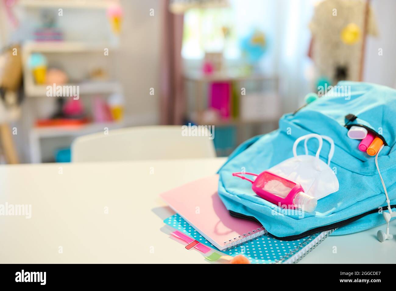 Back to school. Closeup on white table with workbooks, stationary, backpack, ffp2 mask and an antibacterial agent at student room in sunny day. Stock Photo