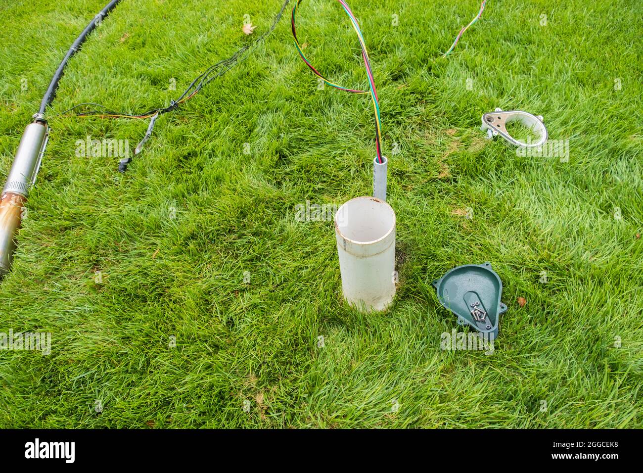 Faulty in ground lawn sprinkler pump  lying in tall fescue grass in the process of being changed out for a new one. A water well wellhead. Stock Photo