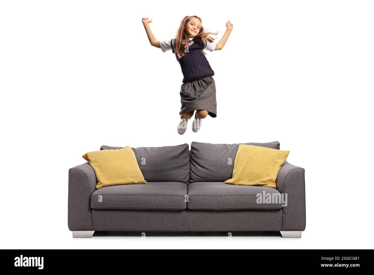 Happy schoolgirl in a uniform jumping on a sofa isolated on white background Stock Photo