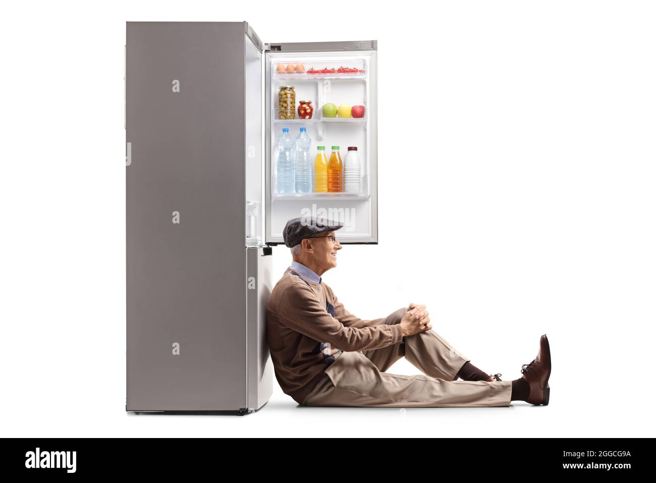 Elderly man sitting on the floor and leaning on a fridge isolated on white background Stock Photo